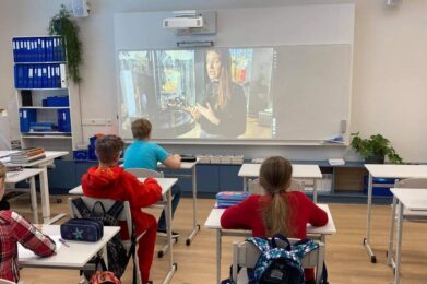 Klassituba õpilastega, kes vaatavad seinale kuvatud videopilti muuseumitöötajast ja nukkudest