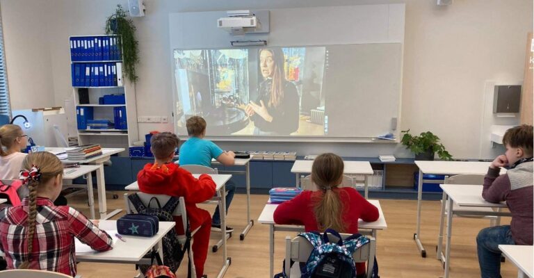 Klassituba õpilastega, kes vaatavad seinale kuvatud videopilti muuseumitöötajast ja nukkudest